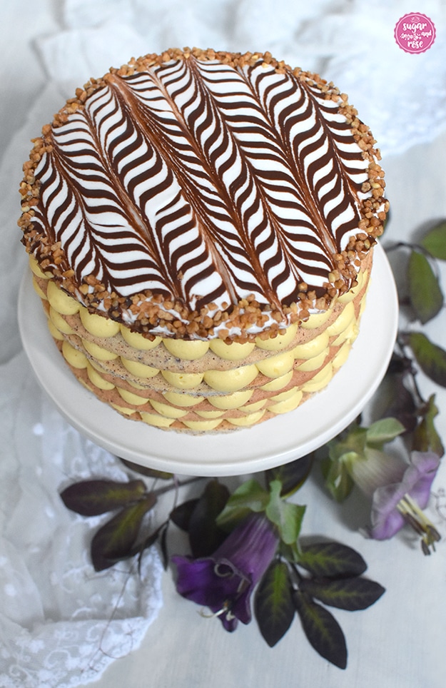 Esterházy-Torte auf weißer Etagere, dekoriert mit lila Blüten der Glockenrebe