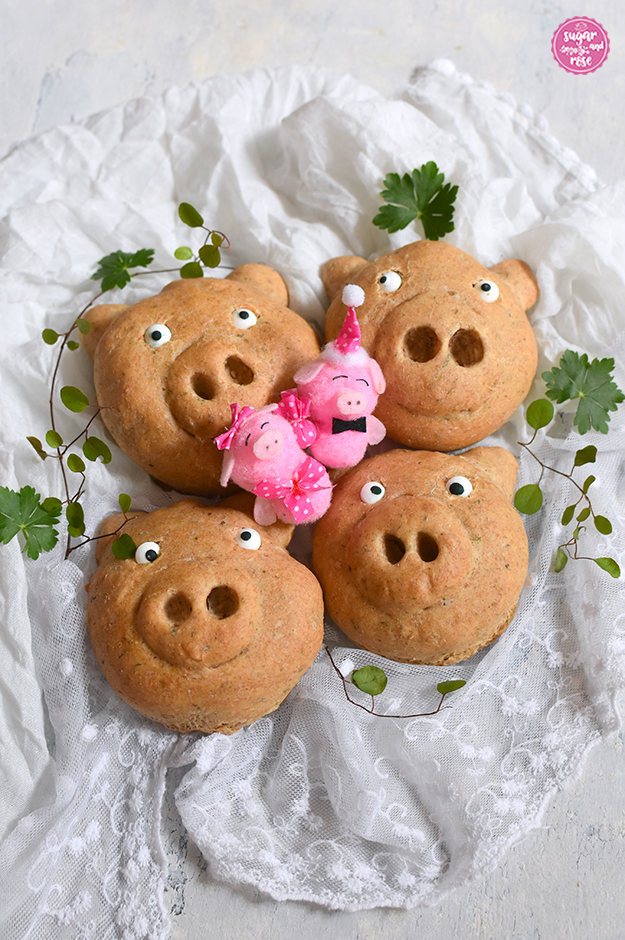 Vier Glücksschweinderl-Brötchen auf weißem Spitzentuch, dekoriert mit zarten grünen Bättern und zwei rosa Glücksbringer-Schweinchen mit rosa Maschen und Hütchen