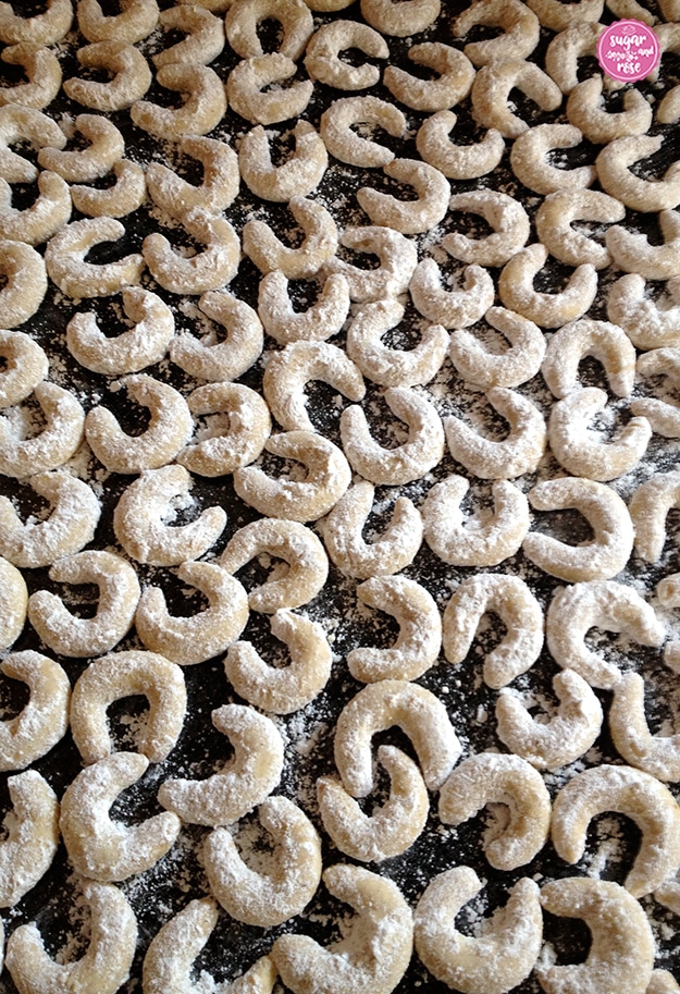 Fertig in Zucker gewälzte Vanillekipferl nebeneinander auf schwarzer Granitplatte zum Abkühlen aufgelegt.