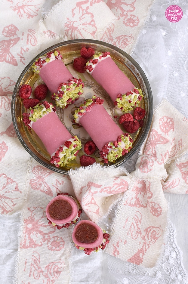 Vier dunkelrosa Punschrullar auf rundem Bauernsilber-Vintageteller, davor eine Rolle in der Mitte durchgeschnitten; man sieht die braune Punschfüllung