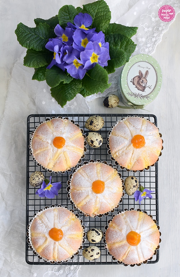 Kuchegitter mit fünf fertigen Blüten-Küchlein mit orangem Marmeladeklecks, dekoriert mit Wachteleiern, lila Blüten und einem lila Primelstöckchen.