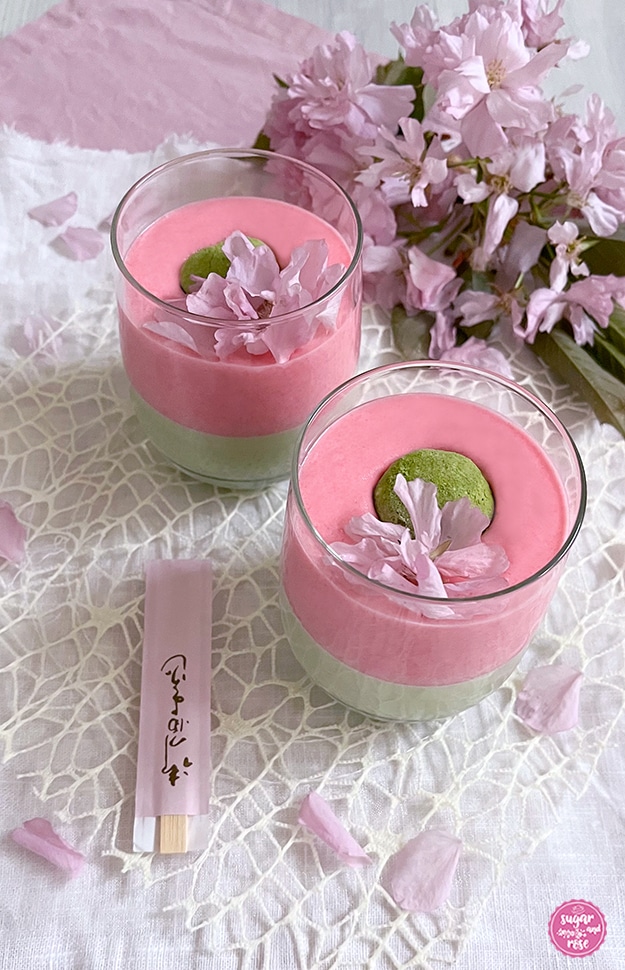 Zwei Gläser mit grün-rosa Matcha-Sakura-Dessert mit grünem Matcha-Mochi und je einer rosa Kirschblüte als Deko