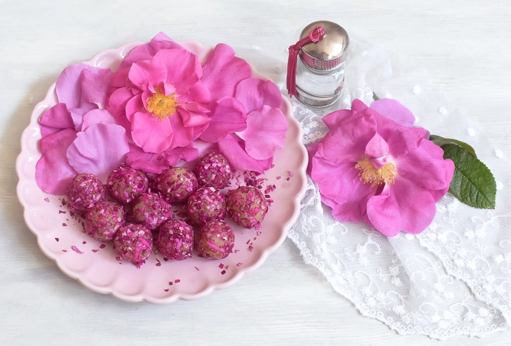 Rosenmarzipan-Kugeln auf rosa Keramikteller mit rosa Rosenblüten auf weißem Spitzentuch