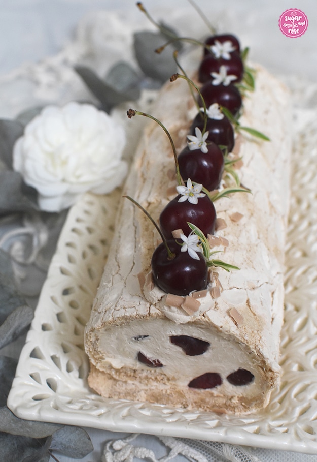 Die Kaffee-Baiserrolle von vorne, im Hintergrund eine weiße Blüte der Rose White Meidiland
