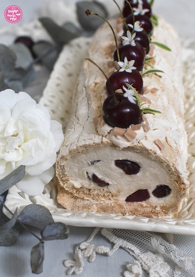 Anschnitt der Kaffee-Baiserolle, tut sichtbar die Kirschhälften. Die Roulade ist mit Karamell-Flakes bestreut.