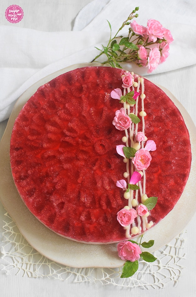 Himbeer-Cheesecake auf rohweißer Steingutplatte mit weißer Leinenserviette und Blüten der Rose The Fairy