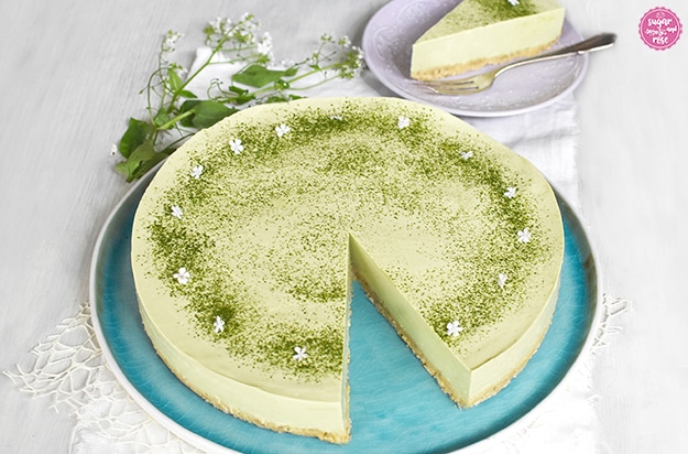 Matcha-Cheesecake in zartem Grün, bestreut mit dunkelgrünem Matcha-Pulver und kleinen weißen Blüten