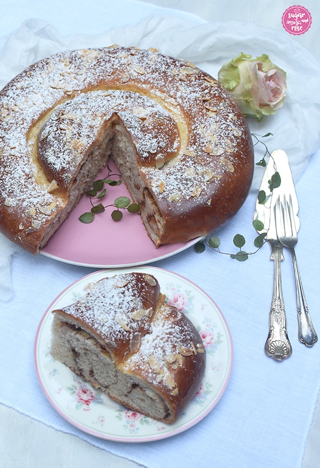 Apfelstrudel-Zimtschnecke angeschnitten auf rosa Teller, davor ein kleiner Teller mit Rosendekor, auf dem ein Stück der Schnecke liegt. man sieht schön die aufgerollten Stränge.
