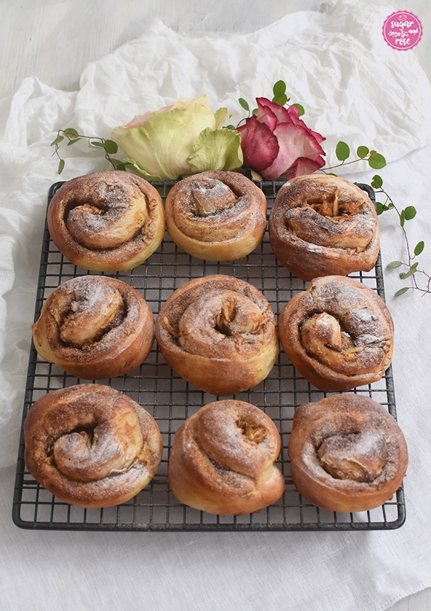 Kleine Apfel-Zimtschnecken auf grauem Gitterrose, fein mit Staubzucker bestreut