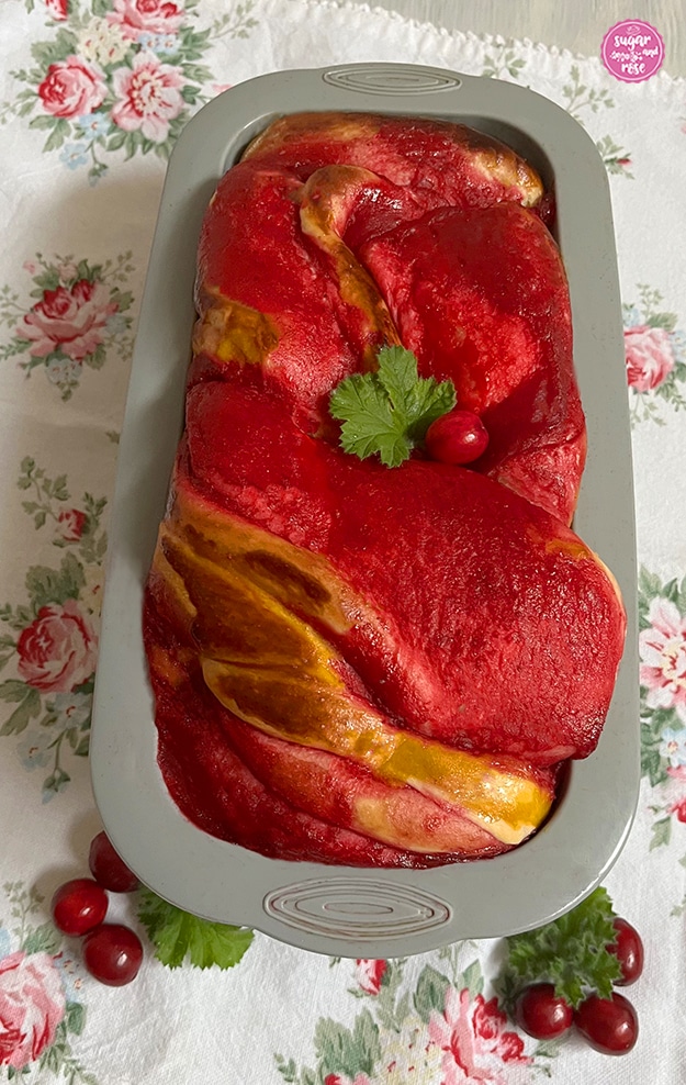 Cranberry-Brioche in grauer Kastenkuchen-Silikonform auf weißer Leinenserviette mit Rosendekor. Im Vordergrund einige frische Cranberrys.