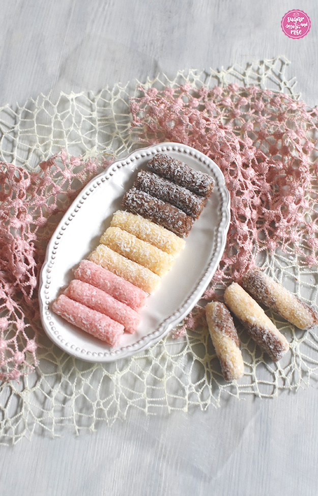 Rosa, weiße und braune Kokosstangerl auf ovalem Keramikteller, davor weiß-braune gedrehte Kokosstangerl