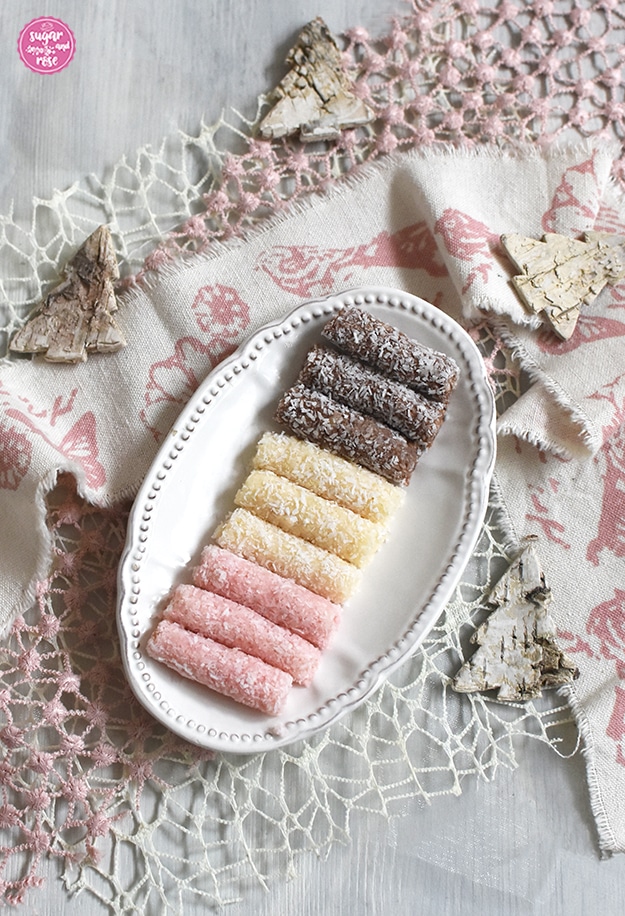 Kleine Kokosstangerl in rosa, weiß und braun auf ovalem kleinen Vintage-Keramikteller, darunter weiß-rosa Leinenbänder und kleine Tannenbäumchen aus weißer Birkenrinde