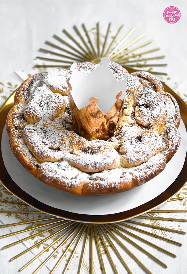Dreikönigskuchen mit Kletzen auf Goldrandteller, in der Kuchenmitte eine goldene Papierkrone, darunter sonnenförmige goldene Untersetzer