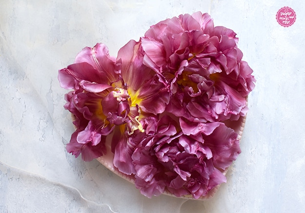 Ein herzförmiger hellrosa Teller, darauf mehrere fuchsia-farbene Tulpenblüten in Herzform arangiert