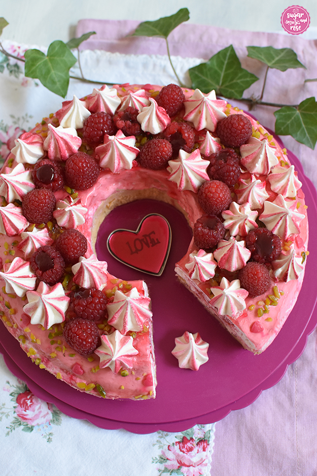Himbeer-Pistazien-Saturntorte angeschnitten, ein Stück fehlt, in der Tortenmitte liegt ein rotes Glasherz mit Aufschrift "Love"