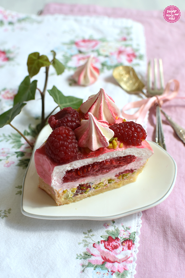 Himbeer-Pistazien-Saturntorte-Tortenstück auf herzförmigem Teller, gut sichtbar im Querschnitt die Himbeerfüllung und die hellgrüne Ganache sowie der Mürbteigboden
