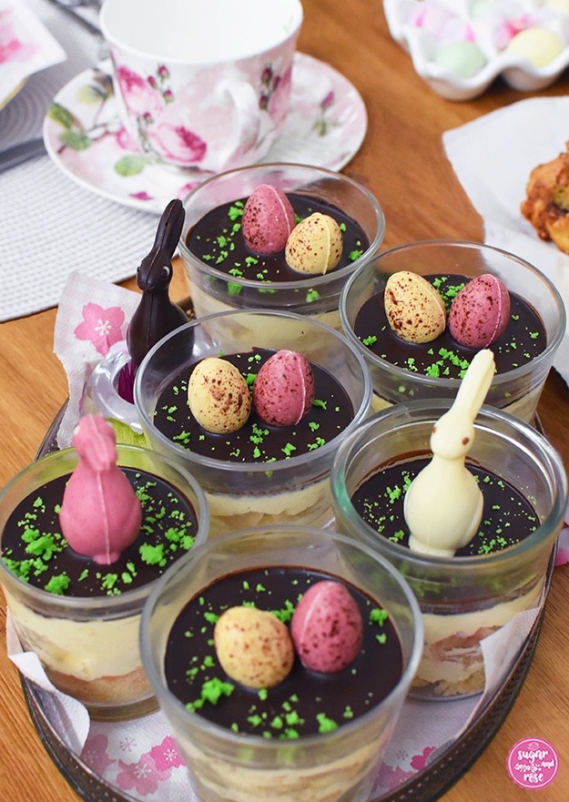 Sechs Gläser Banenschnitten im Glas auf ovalem Silbertablett, dekoriert mit zartgelben und rosa Schokoladenostereiern und ebensolchen Schokoladenosterhasen