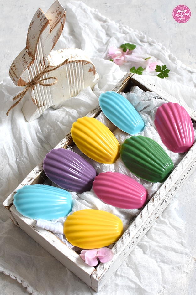 Bunte Eierlikör-Madeleines in weißer Holzkiste, dahinter ein weißer Holzhase im Shabby-Chic-Look