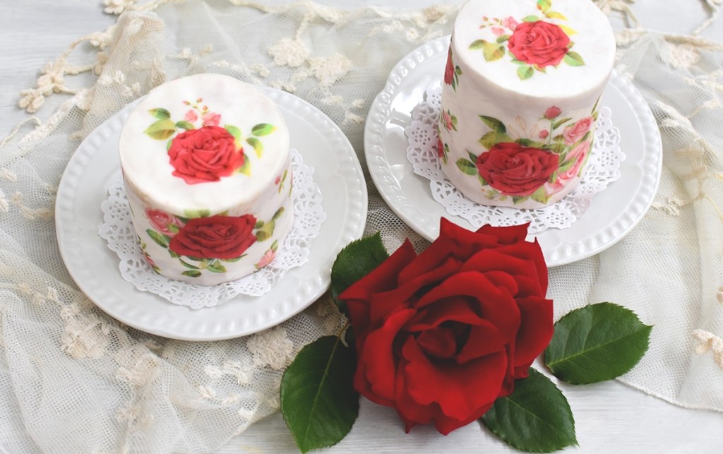 Zwei Rosentörtchen auf weißen Keramiktellern mit einer roten Rosenblüte