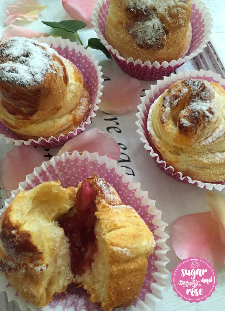 Vier Cruffins in rosa Papiermanschetten, einer in der Mitte auseinander gebrochen