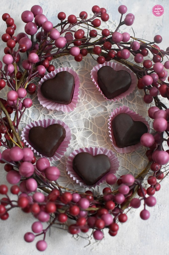 Große Maroniherzen in pinken Pralinenförmchen umrahmt von einem Kranz mit rosa Kügelchen
