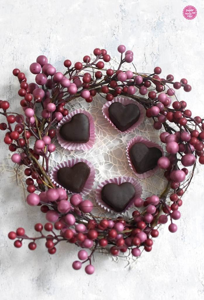 Fünf Maroniherzen in rosa Pralinenförmchen im Kreis aufgestellt, umrahmt von einem Kranz mit rosa Kügelchen