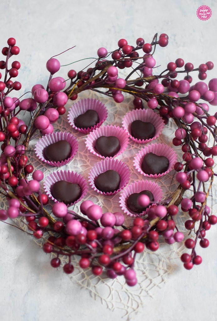 Acht kleinere Maroniherzen in pinken Pralinenförmchen inmitten eines pinken Blütenkranzes