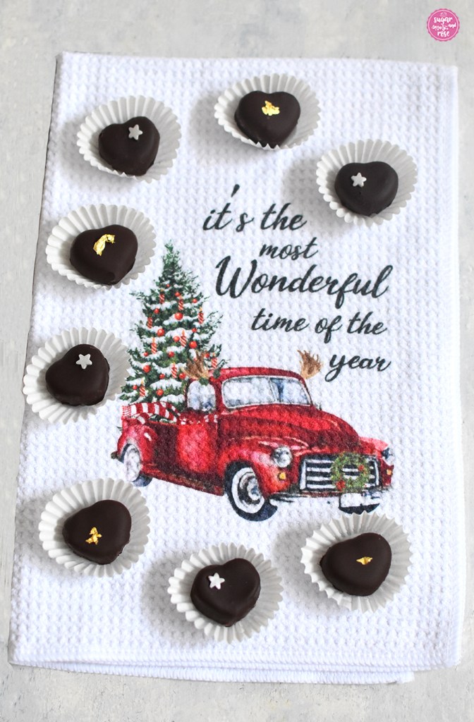 Kleine Maroniherzen in weißen Papiermanschetten, dekoriert mit Silbersternchen beziehungsweise echtem Gold, alle auf einem weißen Geschirrtuch mit einem roten Auto mit Weihnachtsbaum und Beschriftung "It's most Wonderful time of the year"