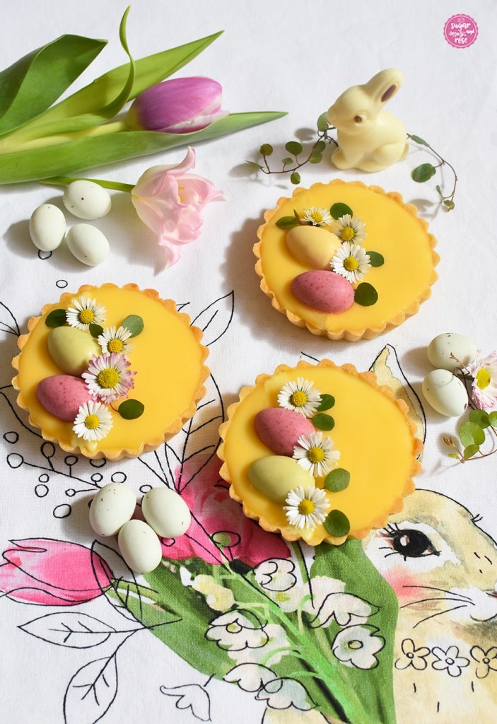 Drei Eierlikör-Tartelettes mit rosa und hellgrünen Schokoeiern und Gänseblümchen dekoriert