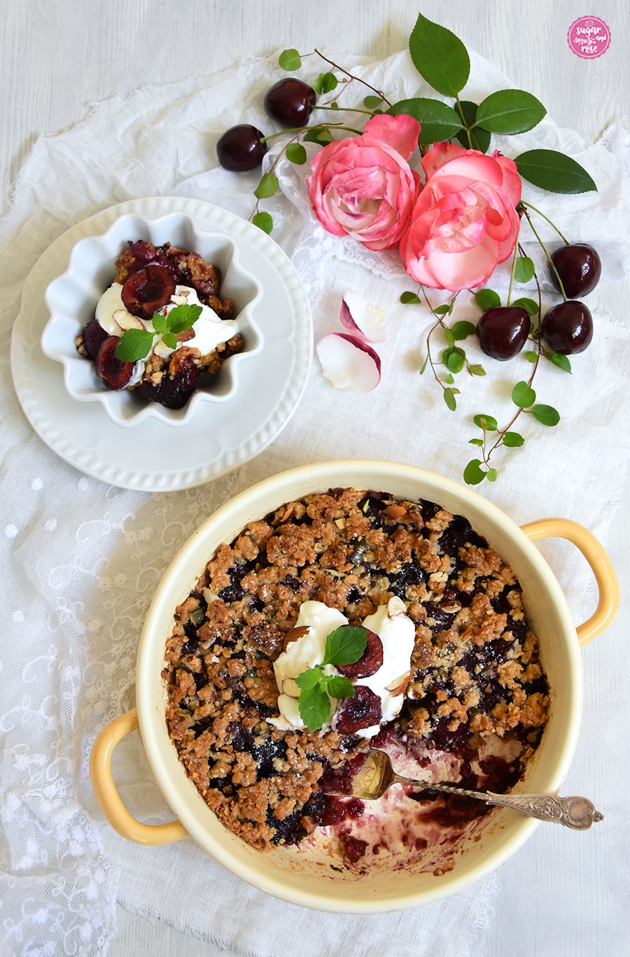 Gelbe Emaillepfanne mit gebackenem Crumble, eine Portion ist herausgenommen und in einer weißen Porzellanschale angerichtet