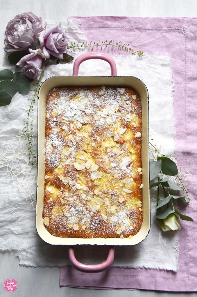 Apfelschedl gebacken in rosa Riess-Emaille-Pfanne (Rein) mit zwei Griffen, daneben drei lila Rosenblüten und silbergrüner Eukalyptus