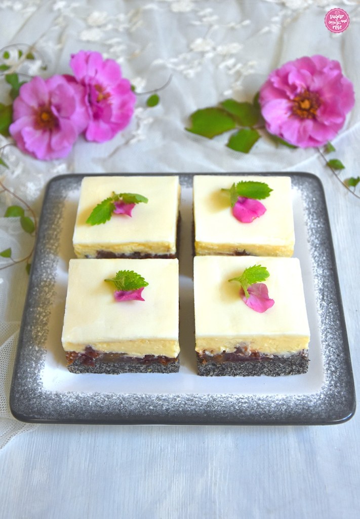 Vier Stück Mohn-Zwetschken-Kuchen mit Vanillecreme auf eckigem weißen Gmundner Teller mit grauem Rand, im Hintergrund rosa Blüten der Rosa Orienta Djamila