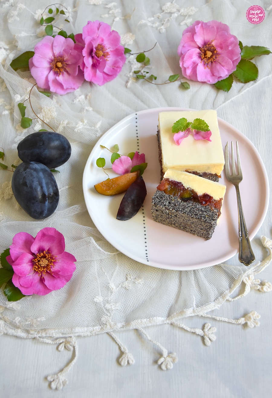 Zwei Stück Mohn-Zwetschken-Kuchen mit Vanillecreme auf einem rosa-weißen Teller, ein Stück umgelegt, sodass die einzelnen Kuchenschichten gut sichtbar sind: Mohn, Zwetschke, Creme und Glasur