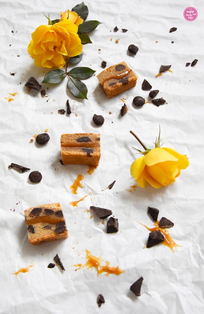 Drei kleine Karamell-Cookies-Stücke auf Papier, dazwischen Schokoladenstücke und klebriges Karamell
