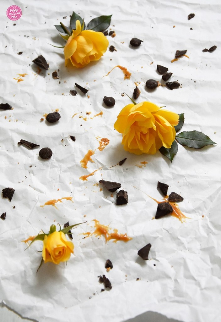 Alle Karamell-Cookies aufgegessen, übrig nur das weiße Papier, Schokostückchen und Karamellflecken sowie drei gelbe Rosen