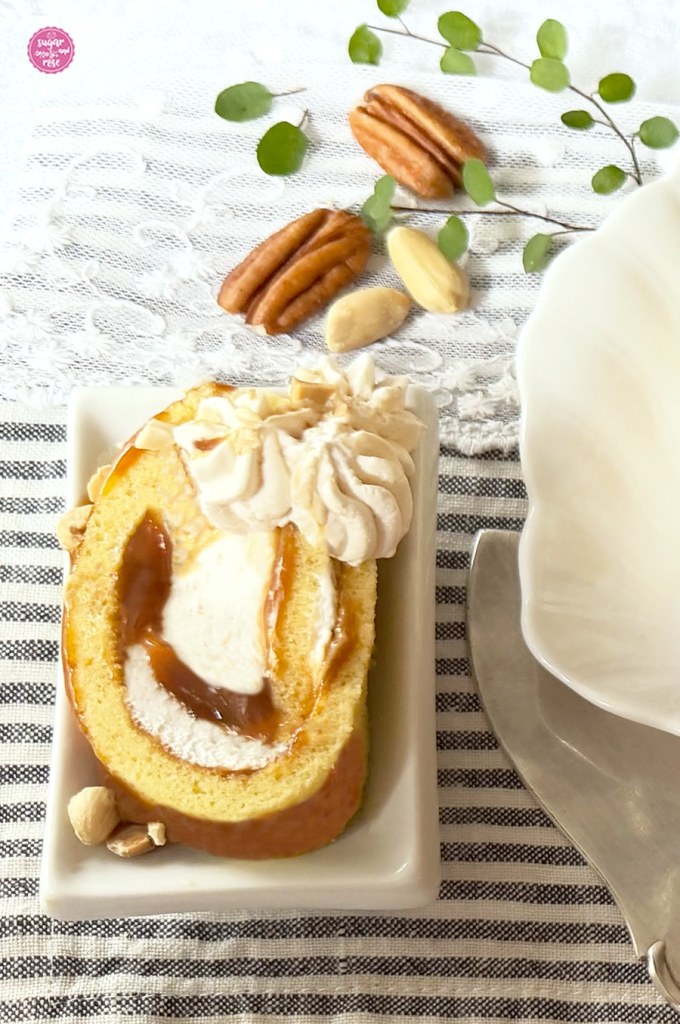 Ein Stück Karamell-Biskuitrolle auf rechteckigem weißen Porzellanteller, aus dem Kuchen quillt der Karamell heraus
